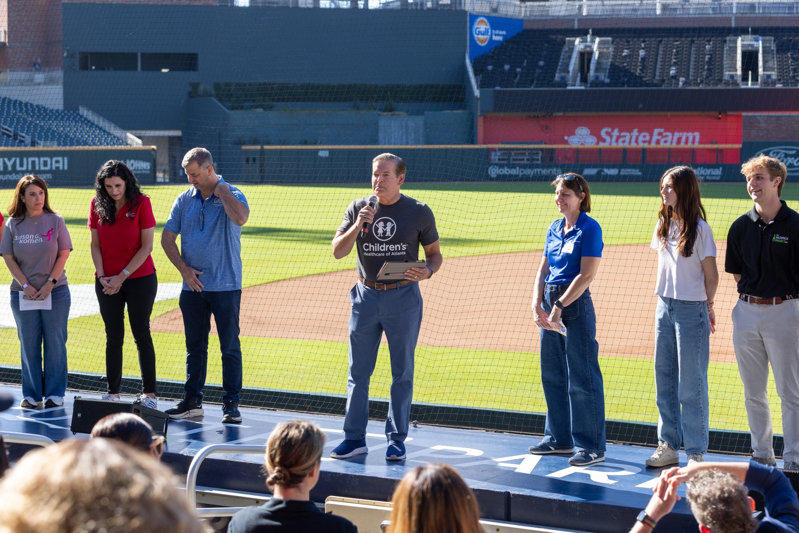 A Backpack Project polo wearer stands with partners on the Truist Park field during a recognition moment.