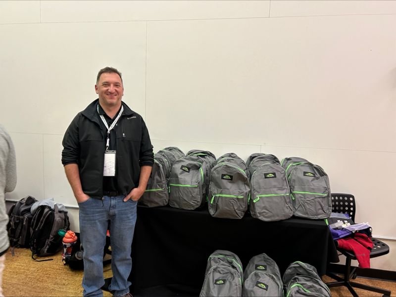 A volunteer smiles beside packed backpacks at an Oldcastle packing.