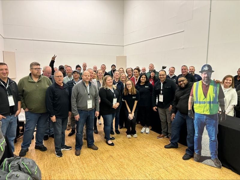 A large Oldcastle volunteer group poses indoors with backpacks in the foreground.