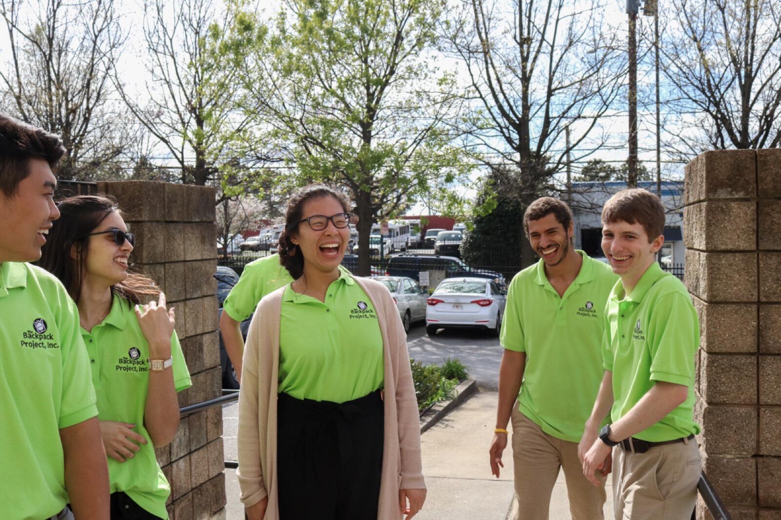 Volunteers in green polos laugh together before a distribution.